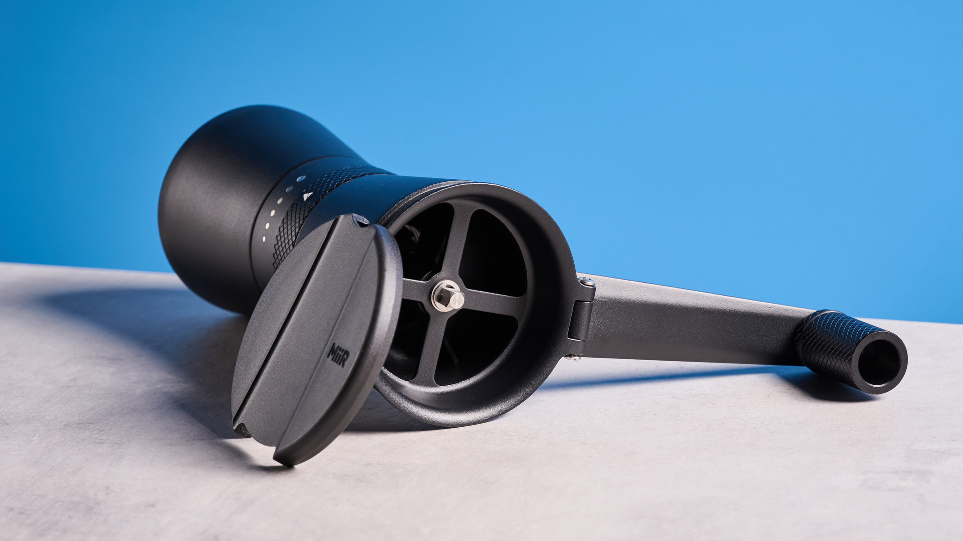 MiiR New Standard Hand Grinder in matte black photographed in front of a blue background