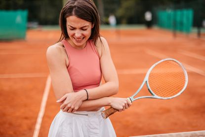 Living with chronic pain: Woman holding elbow in pain while playing tennis