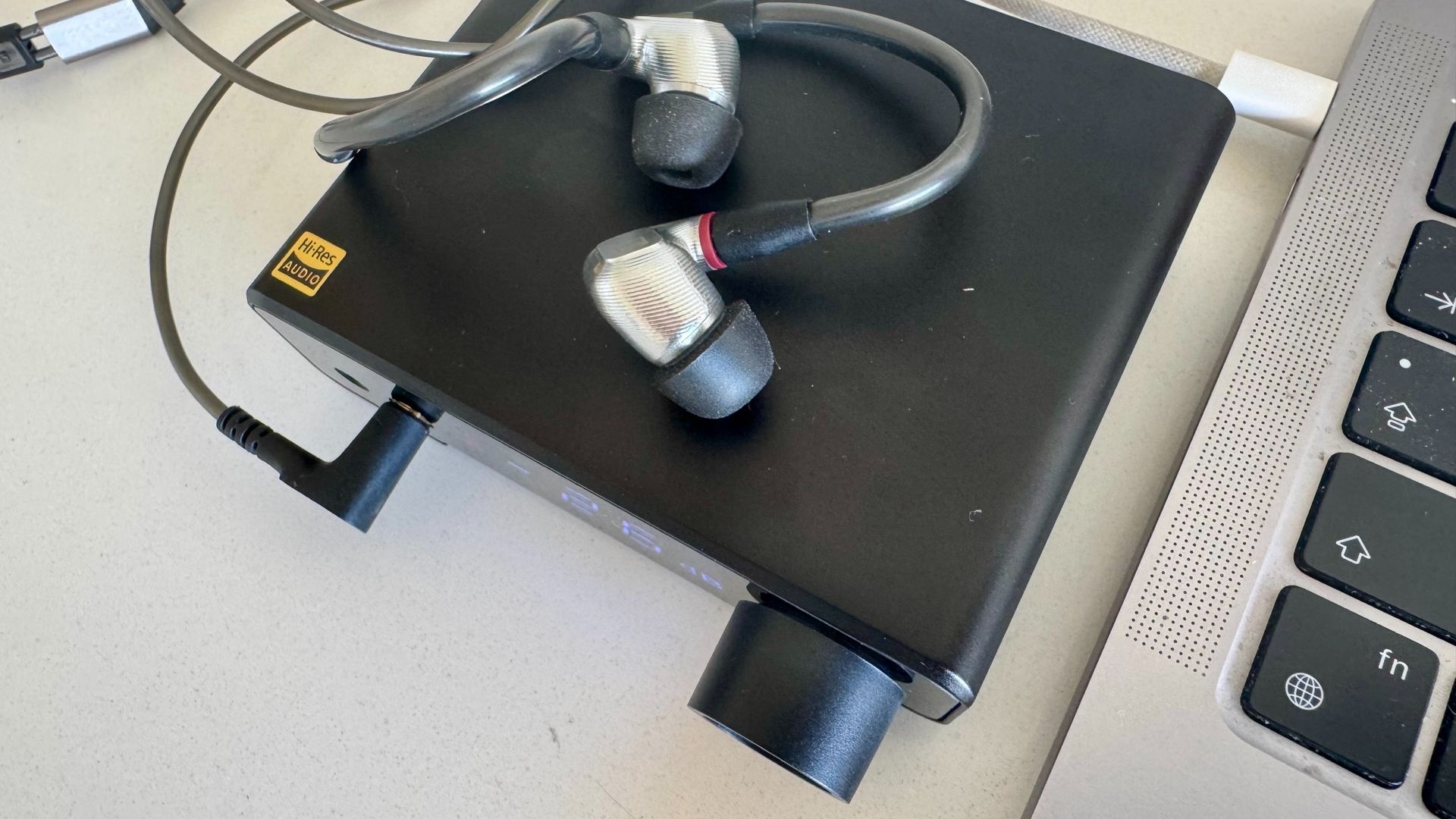 A bird's eye shot of the Topping DX1 II DAC, next to a laptop and on a white surface