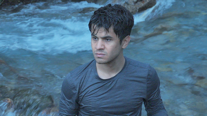 A man looking determined by a river in the woods