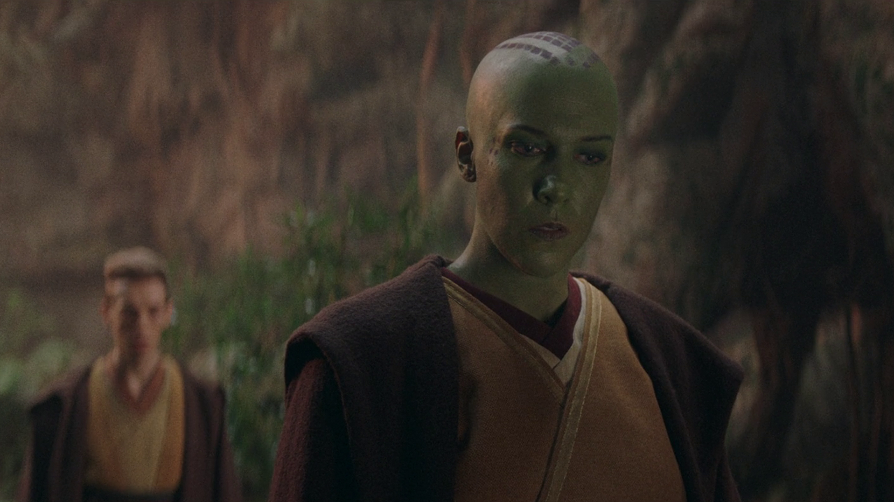 A jedi with a mostly shaved head is in the foreground. Behind them is a younger jedi. Both are wearing brown robes.