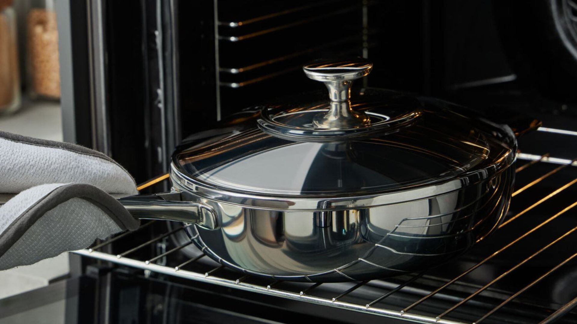 Lakeland 10-in-1 Tri-Ply Only Pan Pro on a white background being placed onto a tray in the oven with oven gloves