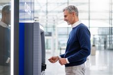 A middle aged man withdraws money from an ATM.