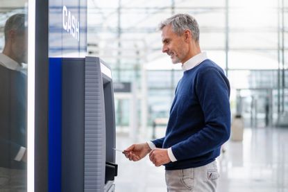 A middle aged man withdraws money from an ATM.