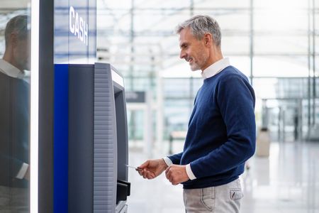 A middle aged man withdraws money from an ATM.