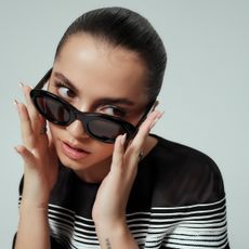 Isabela Merced poses wearing black sunglasses and black and white stripe Chanel dress. 