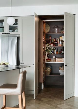 A pantry cupboard painted a super light green color. Inside it are open shelving with lots of food and snacks.