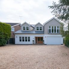 New England style house with cladding and rendered exterior and dormer windows with a large gravel driveway