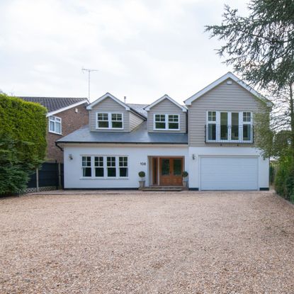 New England style house with cladding and rendered exterior and dormer windows with a large gravel driveway