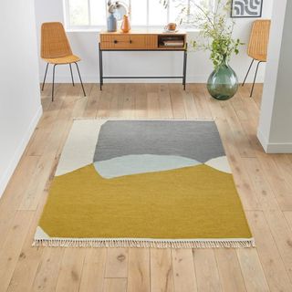 A graphic wool rug with mustard, gray, blue and white sections on wooden floor