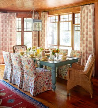 colorful dining room with duck egg grey dining table, patterned covered dining chairs, patterned drapes, rug, lantern, varnished shiplap on walls and ceiling, wooden floor