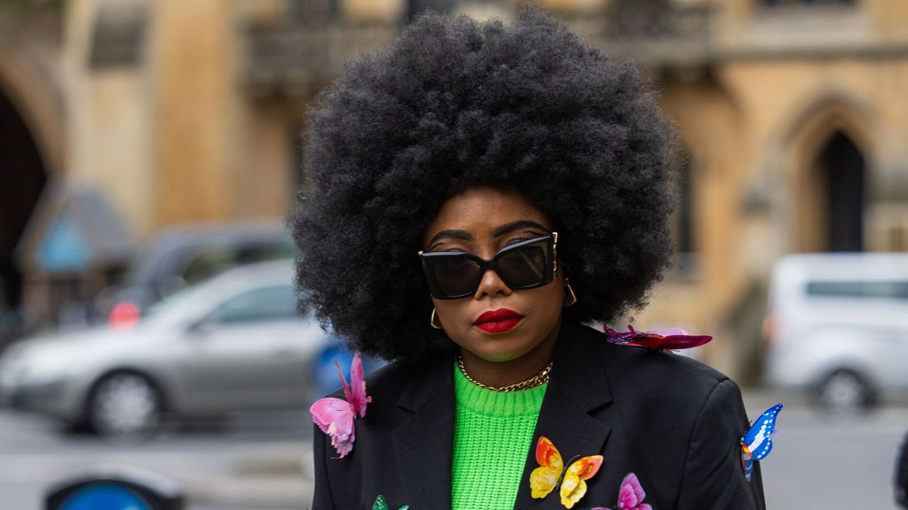 Black woman with natural textured hair wearing blazer covered in butterflies and sunglasses - gettyimages 2018778445