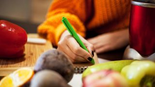 Person writing list surrounded by fresh groceries