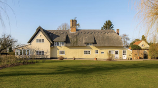 A large beige home with a thatched roof with a large lawn