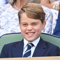 Prince George grins while attending Wimbledon and wearing a navy suit with a white shirt and striped tie