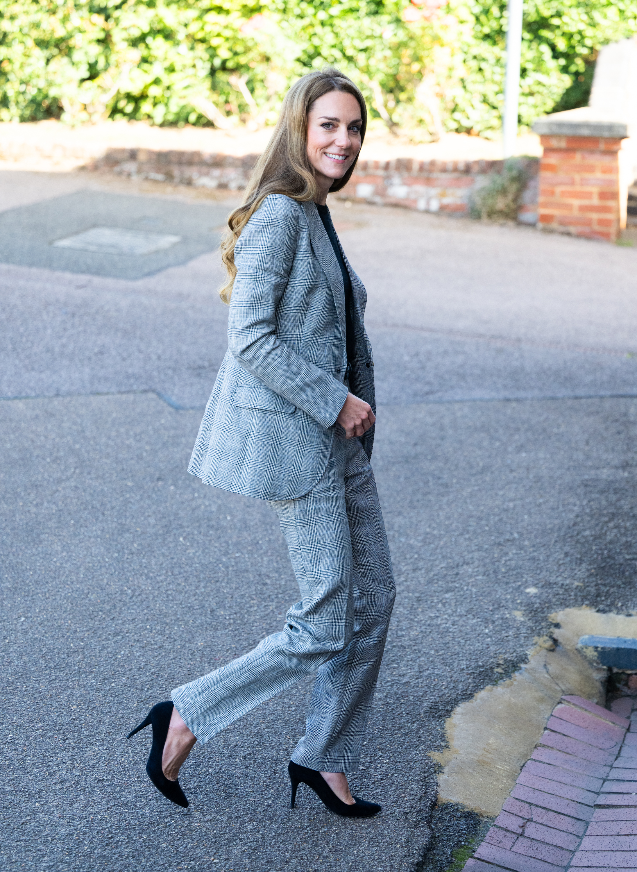 Kate Middleton wearing a gray suit and black heels walking outside