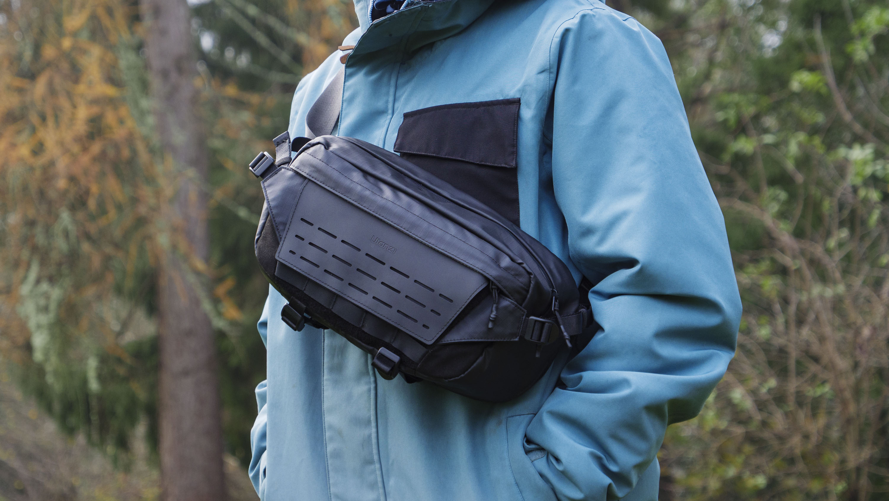 Man wearing a blue jacket outside with a Ulanzi Camera Sling Bag over his shoulder and resting on his midriff