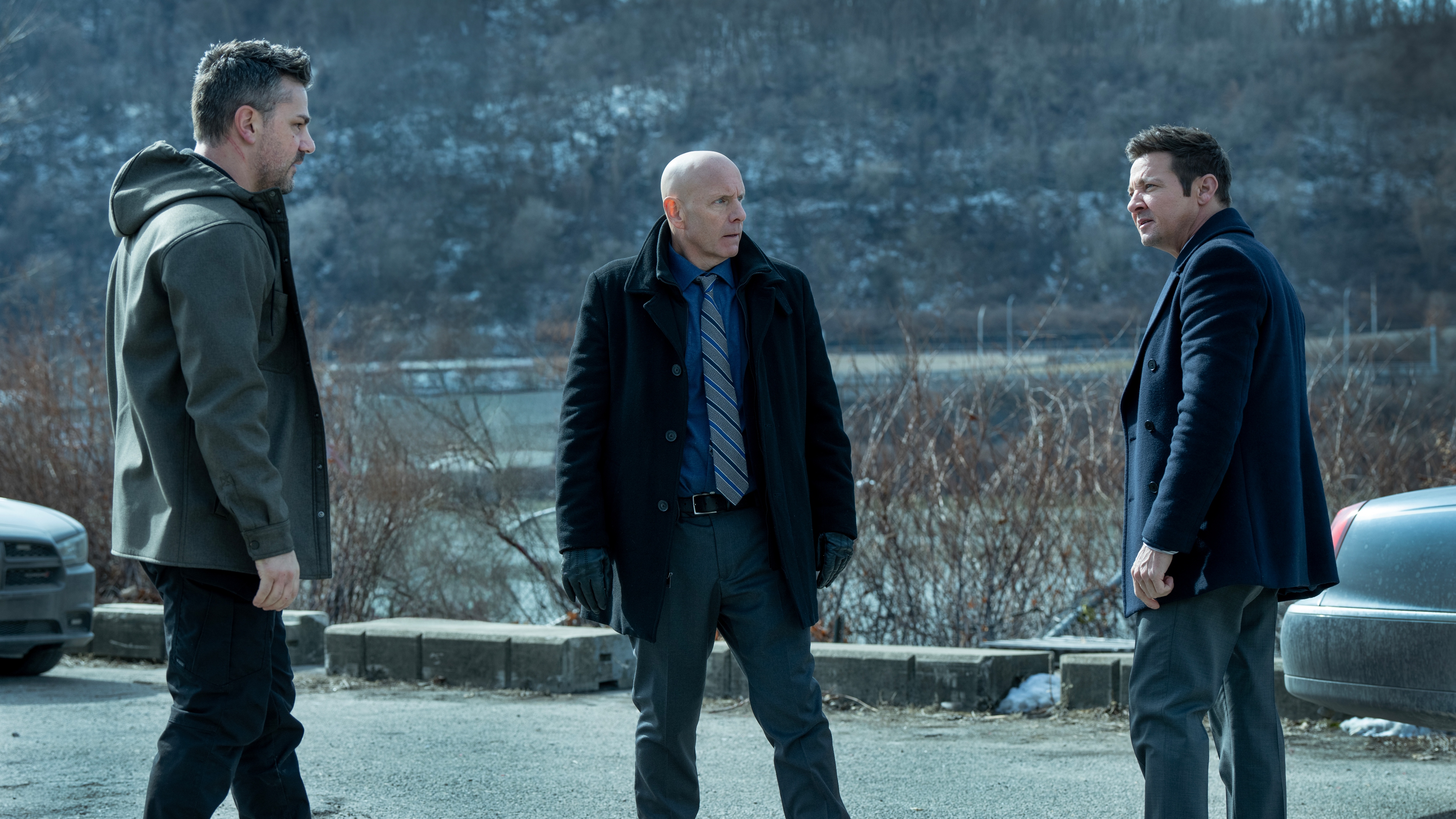 L-R: Hamish Allan-Headley as Robert, Hugh Dillon as Ian and Jeremy Renner as Mike McLusky standing and looking at each other wearing suits.