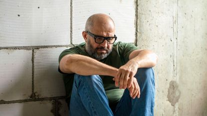 Frustrated man sitting on floor in front of concrete wall