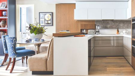 Kitchen and dining area with grey, white and wooden units. Dining table with neutral coloured bench seating and blue and white upholstered chairs. 