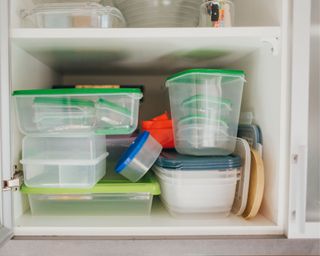 A disorganized cabinet full of tupperware containers with green lids