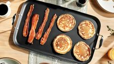 HexClad Hybrid Griddle with pancakes and bacon on it, on a wooden dining table. 