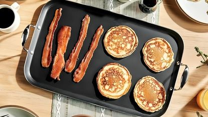 HexClad Hybrid Griddle with pancakes and bacon on it, on a wooden dining table.