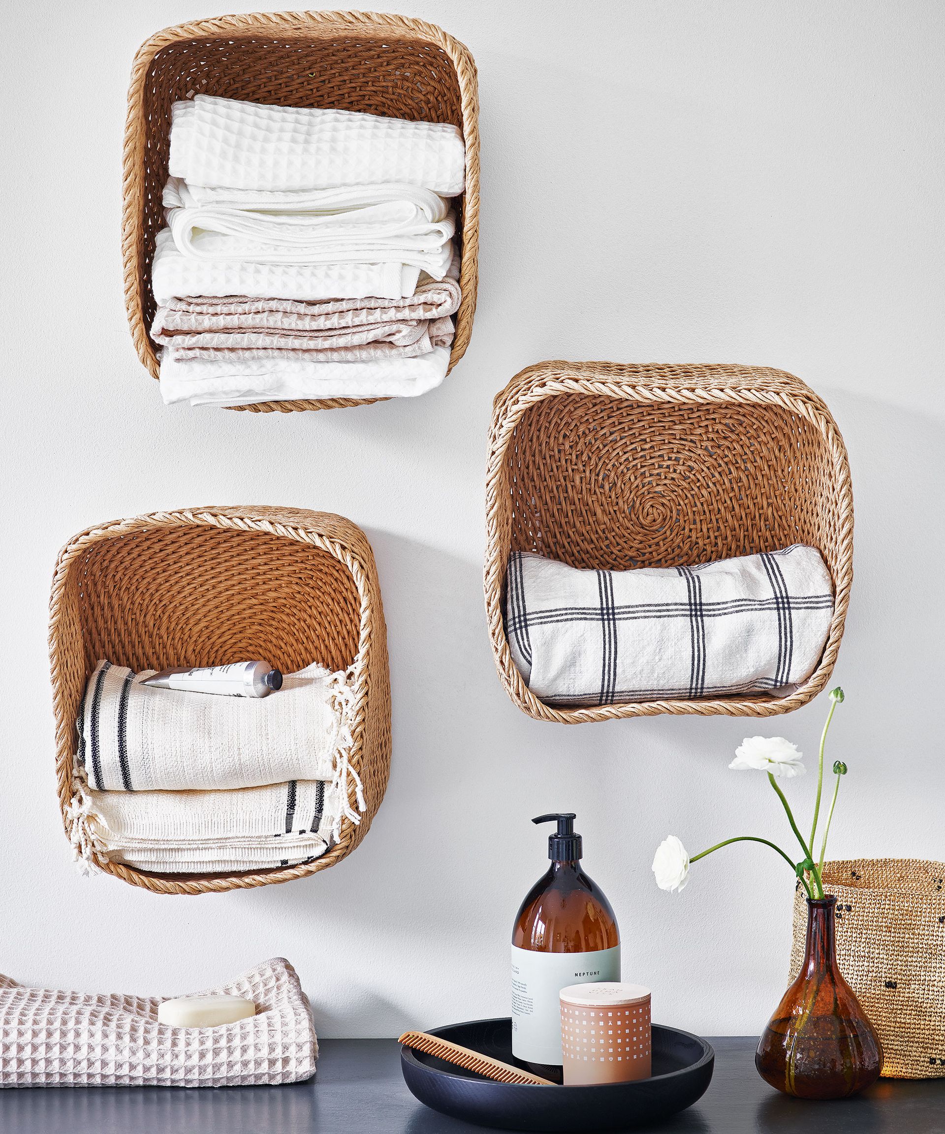 Trio of woven baskets on the wall of the bathroom with stacks of towels folded inside