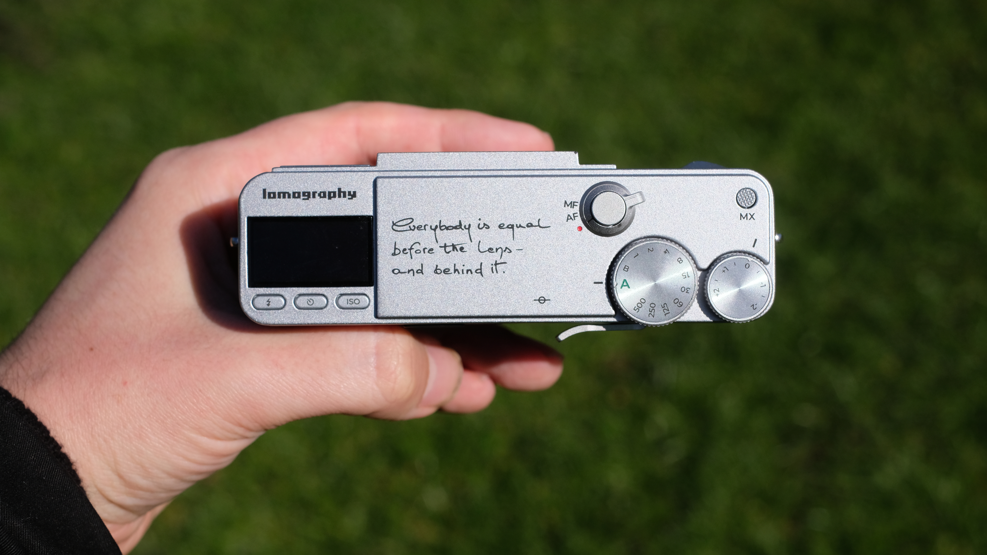 Photograph of the Lomography Lomo MC-A, with grass visible in background, showing detail of top plate with controls and LCD screen