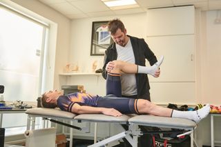 Phil Burt checking the flexibility of a male cyclist by pushing the cyclists' knee towards his hip