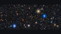 Image of space showing a black sky with hundreds of white dots and a few red, orange, gold and blue dots with halos of light surrounding them. 