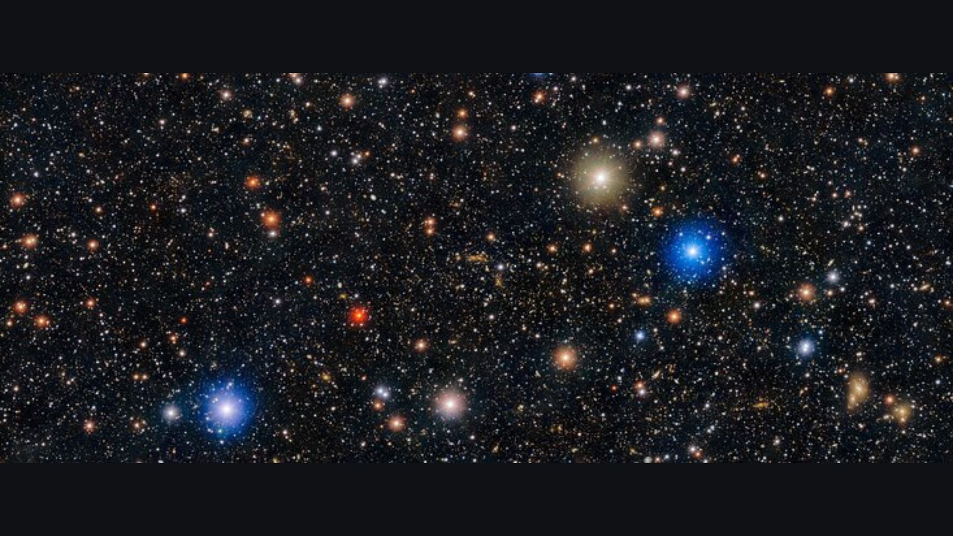 Image of space showing a black sky with hundreds of white dots and a few red, orange, gold and blue dots with halos of light surrounding them.