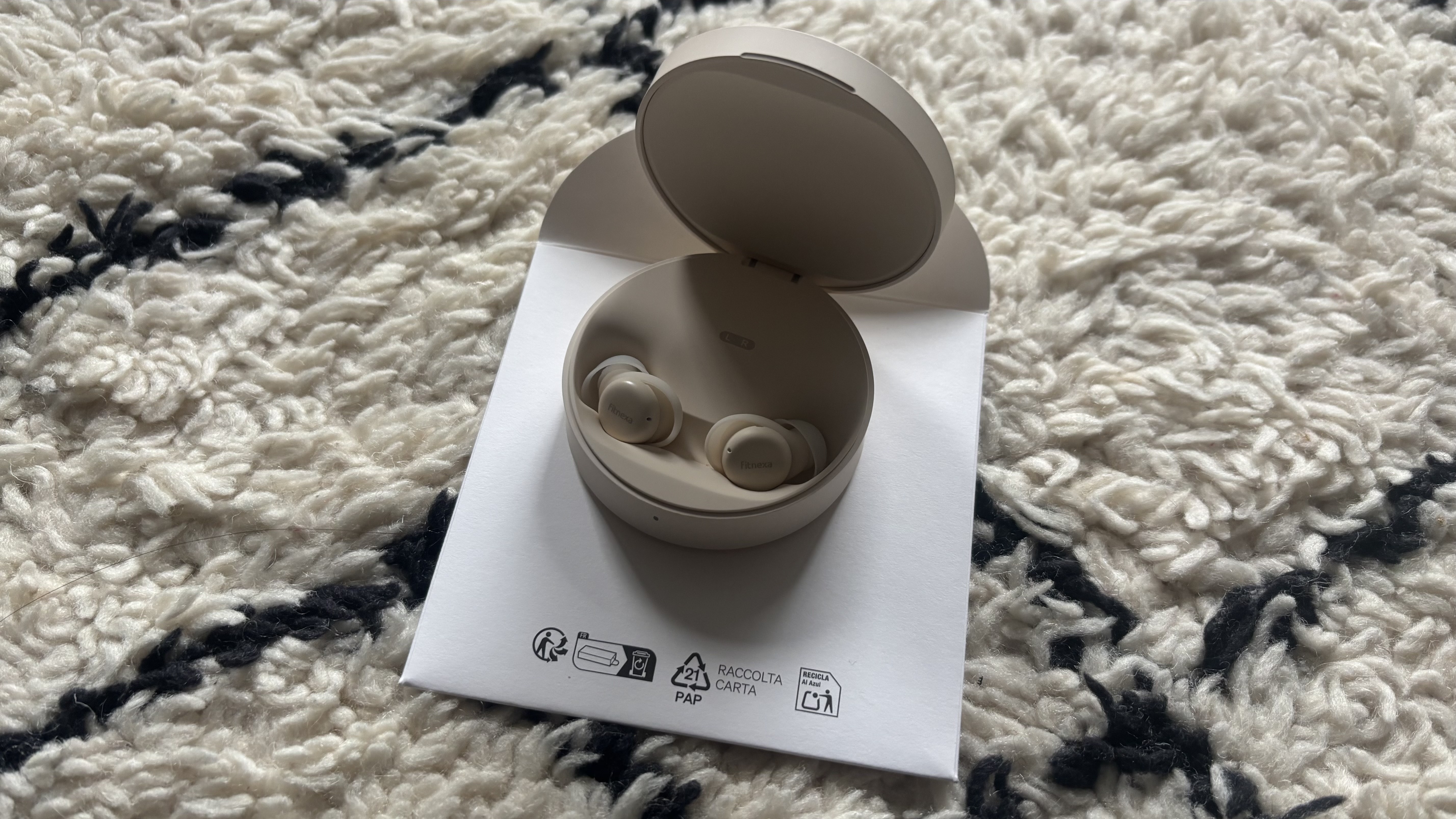 A picture of a recently unboxed pair of Fitnexa SomniPods 3, sleep-tracking earbuds, on a black-and-white carpet.