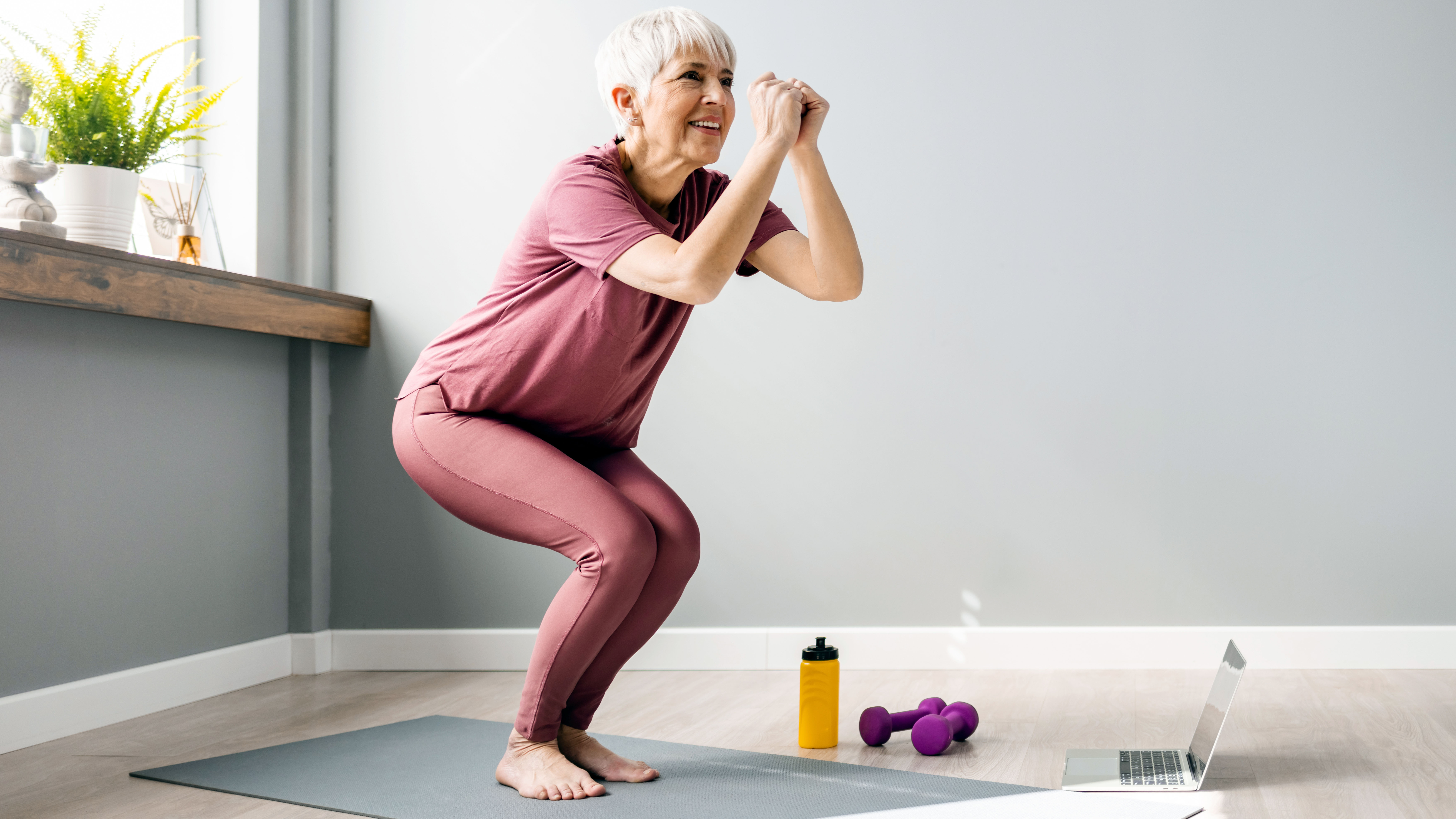 Older woman performing squat at home on yoga mat