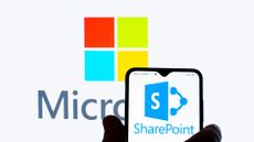 A hand holding a smartphone that has the SharePoint logo, with the Microsoft logo behind it