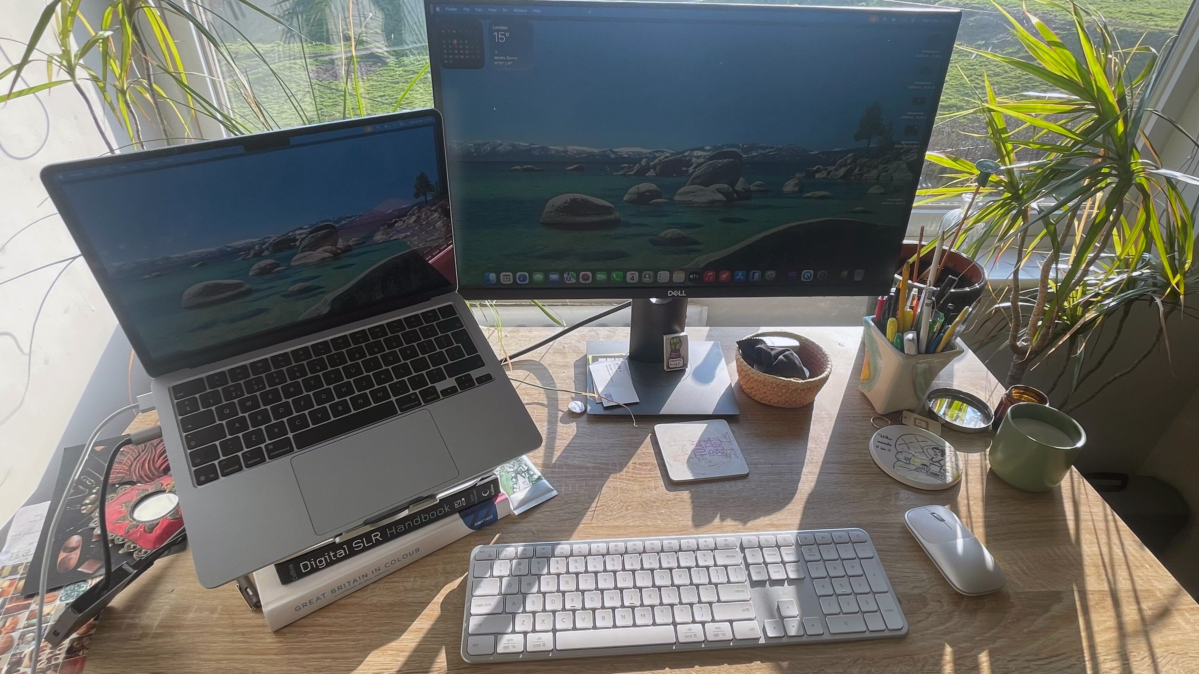 A silver grey Satechi Slim EX3 keyboard and Slim EX mouse on a wooden desk with sunlight shining on it from a window in the background