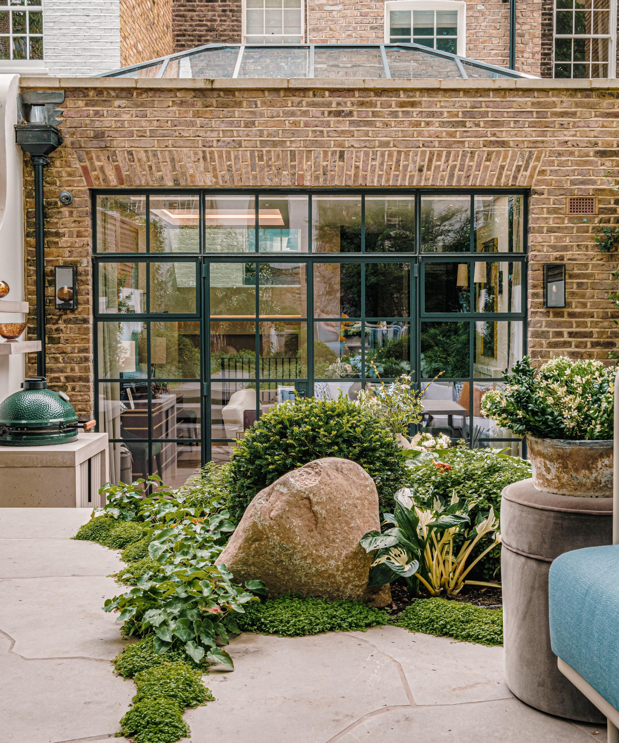 Landscaped back terrace on two levels looking back at the house with a large glass panelled window