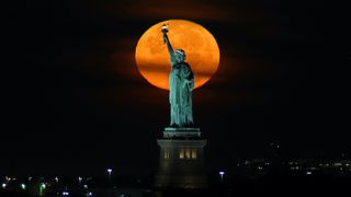 The almost-full Harvest Moon sets behind the Statue of Liberty before sunrise on Sept. 20, 2021