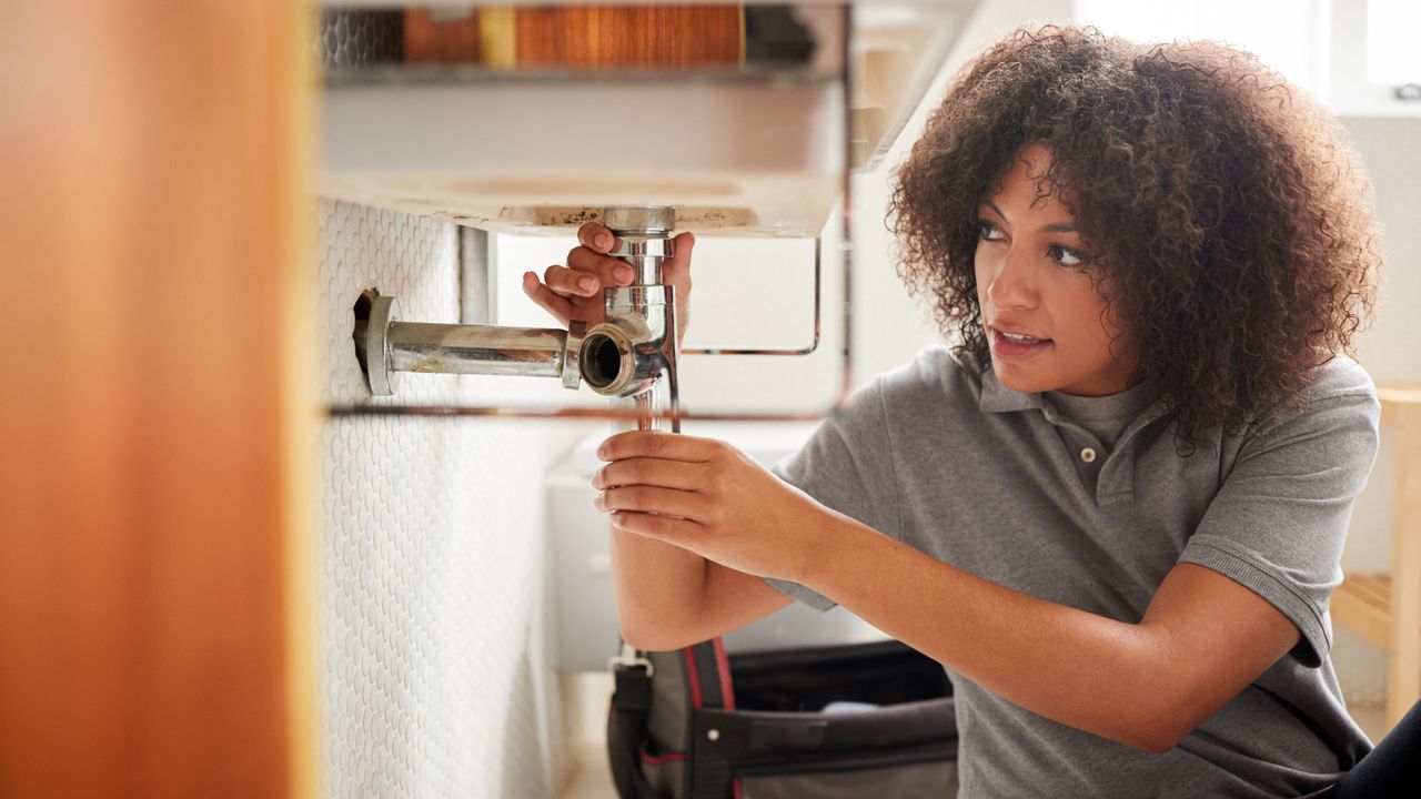 Woman plumber fixing waste pipe under sink