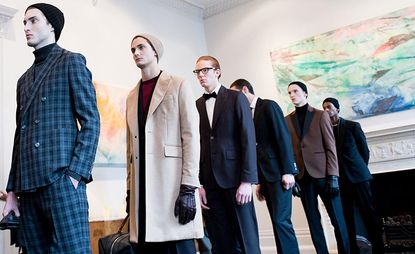 Six models, A single, sharp black and white bow tie suit stood out among the more relaxed silhouettes that paired relaxed turtlenecks under tailored blazers, combined with long tweed coats, often worn closed with a knotted waist tie.