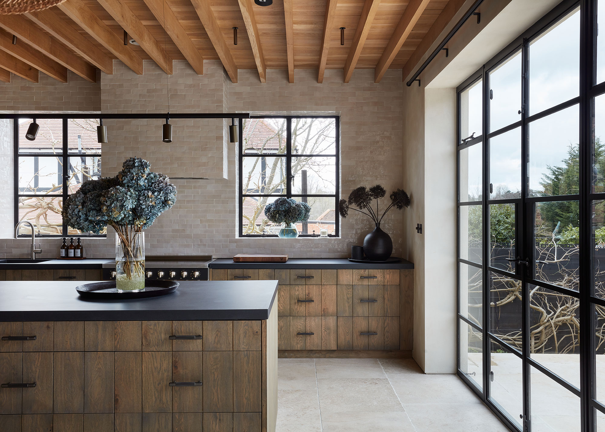 wooden kitchen with Crittal doors leading to the outside. On the island is a large vase with plants inside.