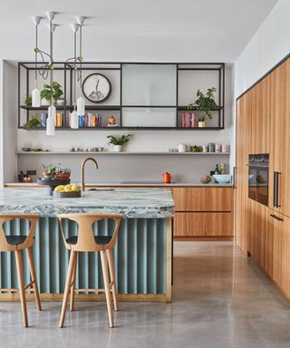 kitchen island color ideas, white kitchen with wooden cabinetry, hanging shelving unit, open shelving, island with fluted aqua base, marble style countertop, bar stools, brass tap, modern feel