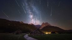 A long exposure shot of the Milky Way and many shooting stars, with the Alps and log cabins in the foreground