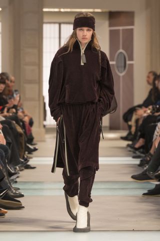 A model wearing a brown velour tracksuit and headband at the Louis Vuitton F/W 25 show.