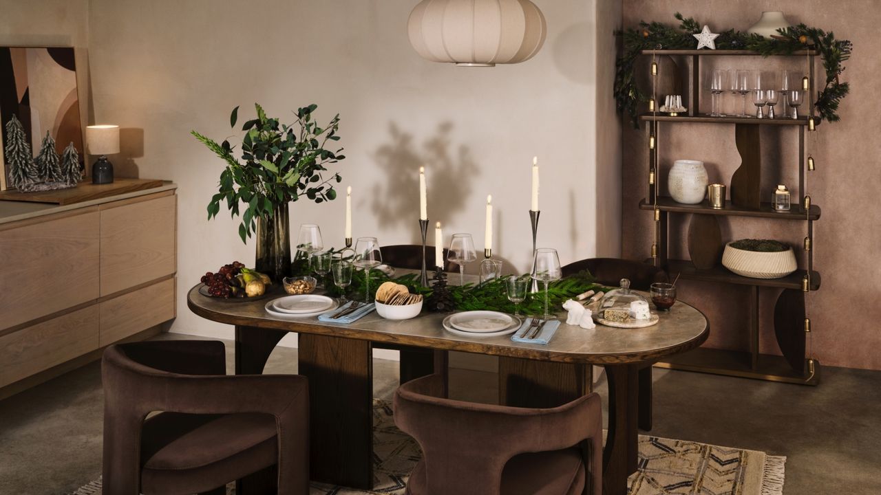 A dining room decorated for Christmas with a oval-shaped table, four brown velvet chairs, and a cabinet 