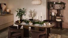 A dining room decorated for Christmas with a oval-shaped table, four brown velvet chairs, and a cabinet 
