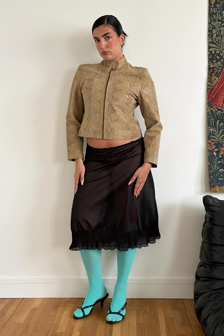 a woman wearing snakeskin leather jacket, black sheer skirt, teal tights, and black sandals
