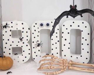 Halloween 'Boo' slogan papier mache sign painted using Dulux white paint with hand painted polka dots. Bat, skeleton hand and pumpkin in background