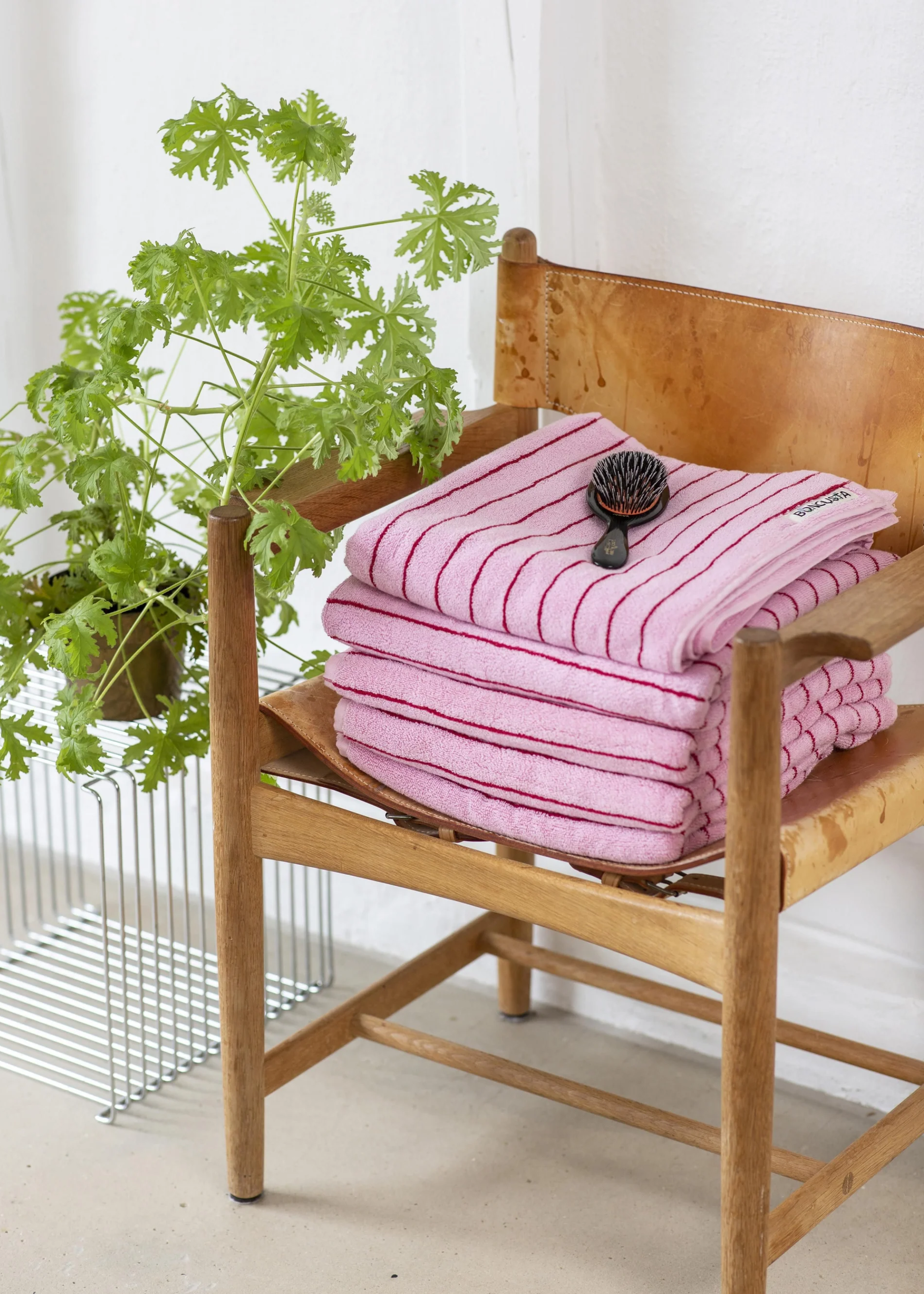 A set of stacked pink and red striped towels on a chair by a potted plant on a steel wire frame