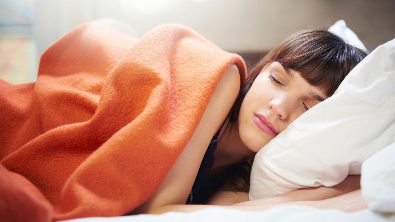 Young woman sleeping under an orange blanket